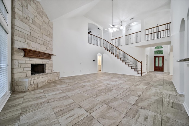 unfurnished living room featuring arched walkways, a fireplace, a ceiling fan, baseboards, and stairs