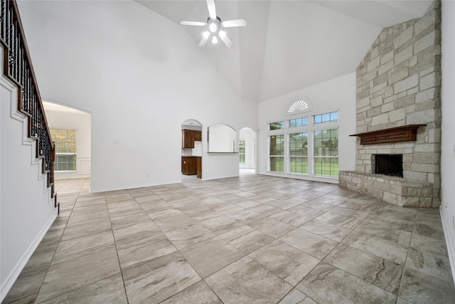 unfurnished living room featuring baseboards, arched walkways, a ceiling fan, stairway, and a fireplace