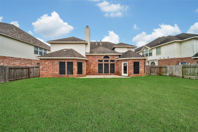 back of property featuring a fenced backyard, a chimney, a lawn, and brick siding