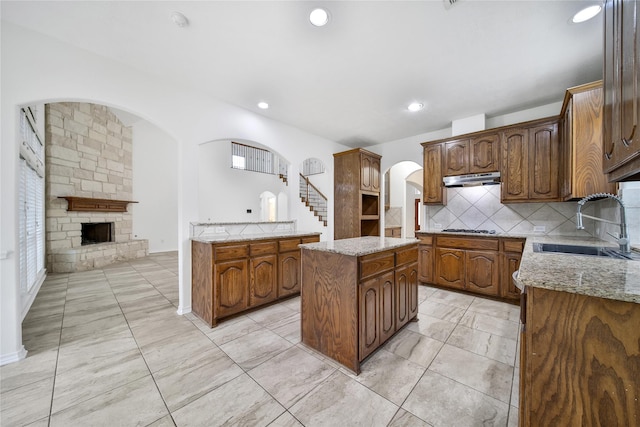 kitchen featuring a stone fireplace, stainless steel gas cooktop, a sink, a kitchen island, and backsplash