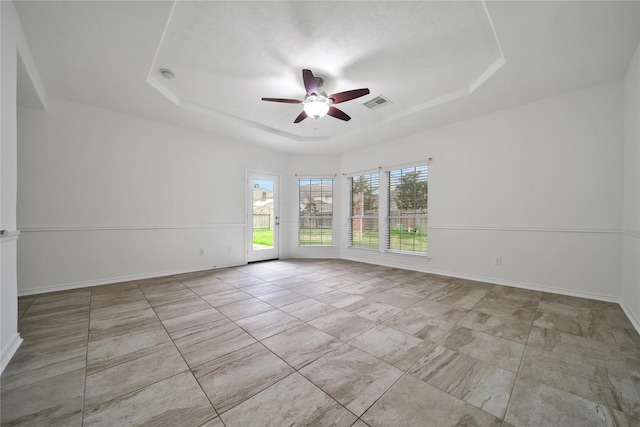 spare room with a ceiling fan, a tray ceiling, visible vents, and baseboards