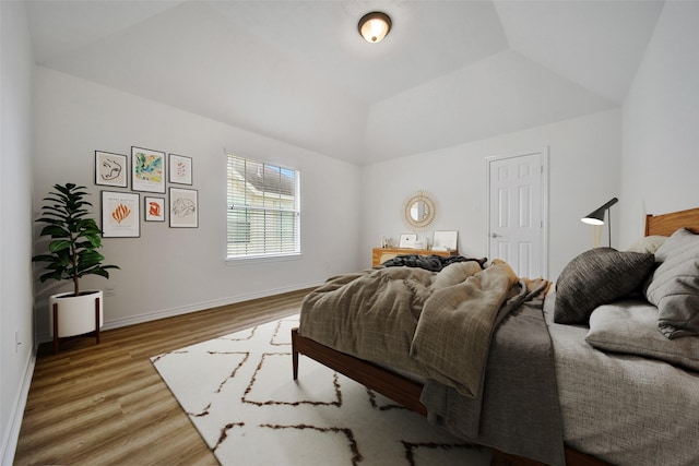 bedroom with vaulted ceiling, wood finished floors, and baseboards