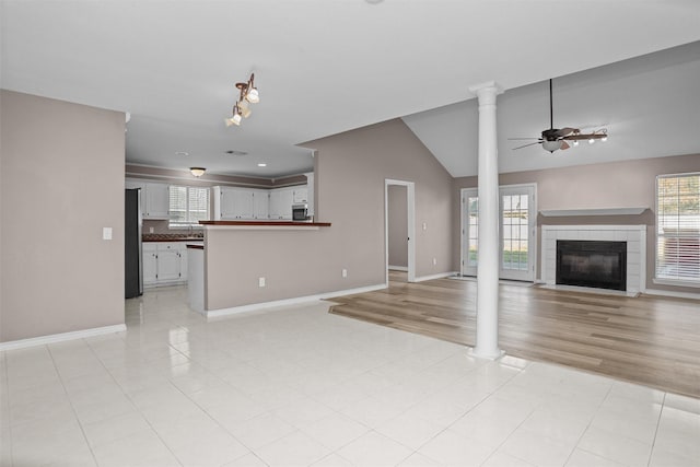 unfurnished living room with a ceiling fan, a tile fireplace, a healthy amount of sunlight, and ornate columns