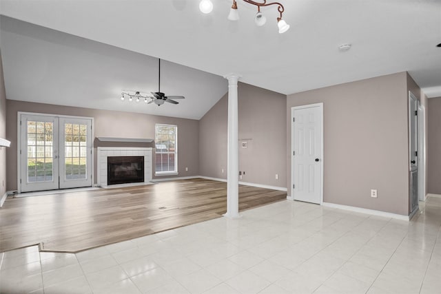 unfurnished living room featuring lofted ceiling, a tile fireplace, a ceiling fan, baseboards, and ornate columns