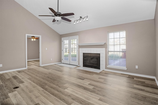 unfurnished living room with high vaulted ceiling, a fireplace, baseboards, french doors, and light wood finished floors