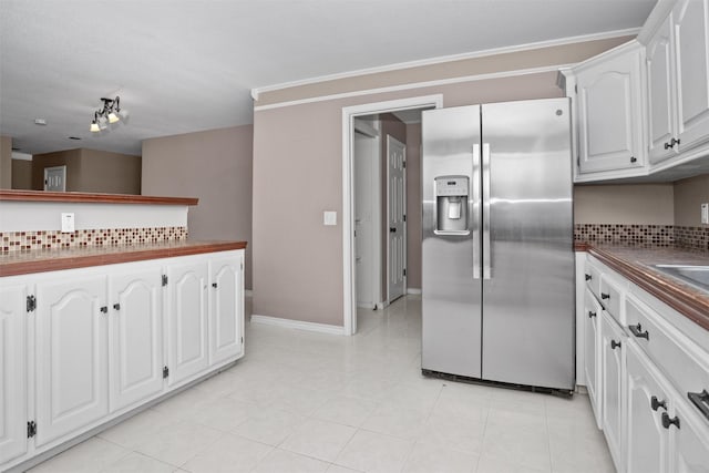 kitchen featuring white cabinetry, tasteful backsplash, dark countertops, stainless steel fridge, and crown molding