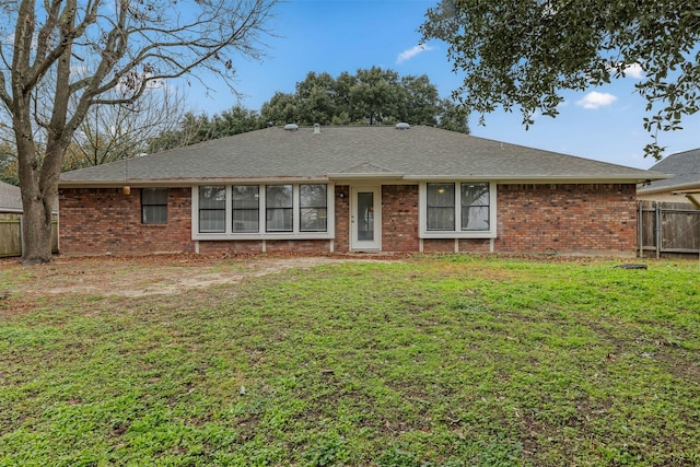 back of house featuring a yard, brick siding, a shingled roof, and fence