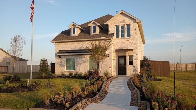 view of front facade with stone siding, a front lawn, a shingled roof, and fence