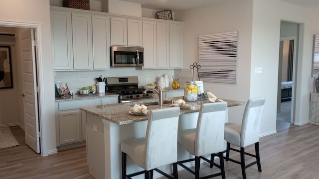 kitchen with a center island with sink, white cabinets, decorative backsplash, a breakfast bar, and stainless steel appliances