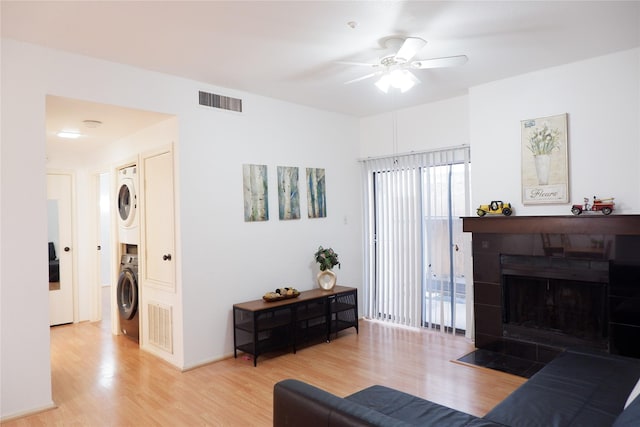 living area with stacked washer and dryer, visible vents, a tiled fireplace, ceiling fan, and light wood-style floors