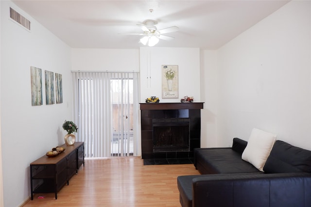 living room with ceiling fan, light wood finished floors, a fireplace, and visible vents