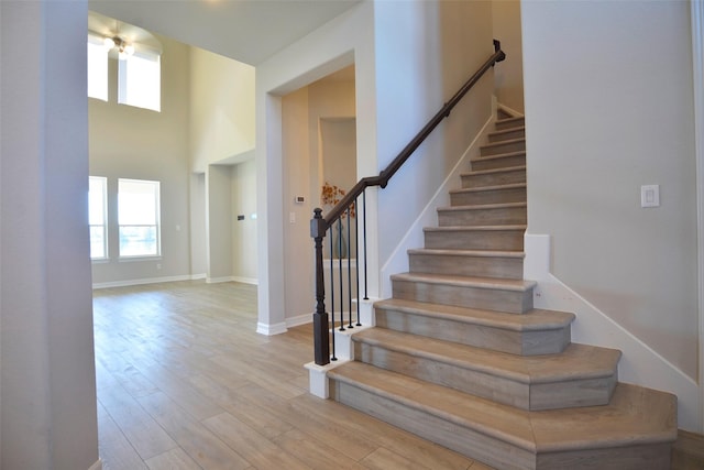 stairway featuring wood finished floors, a towering ceiling, and baseboards