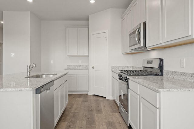 kitchen featuring light wood finished floors, light stone countertops, recessed lighting, appliances with stainless steel finishes, and a sink