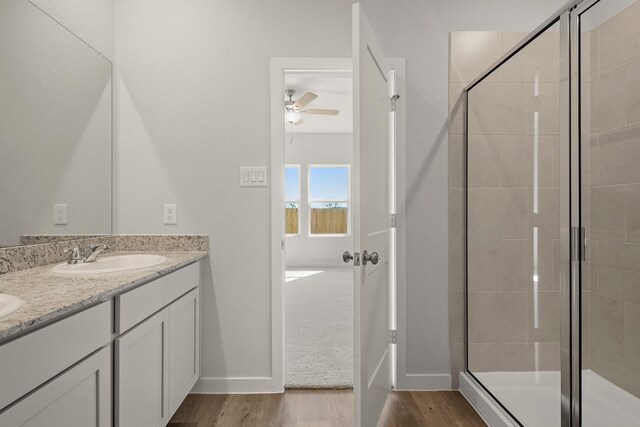 full bathroom with a sink, wood finished floors, a shower stall, double vanity, and ceiling fan