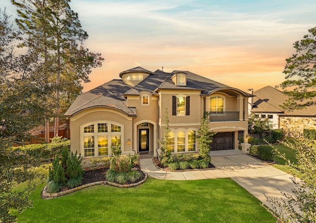 french country style house with a garage, concrete driveway, a front yard, and stucco siding