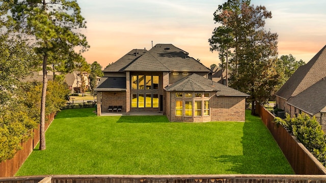 back of property at dusk featuring brick siding, a fenced backyard, a patio, and a yard