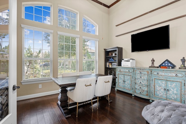 dining room with dark wood-style flooring, crown molding, a towering ceiling, and baseboards