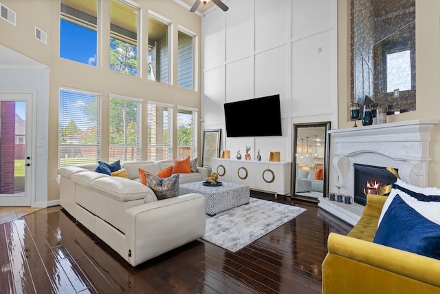 living room featuring a towering ceiling, a warm lit fireplace, visible vents, and dark wood-style flooring