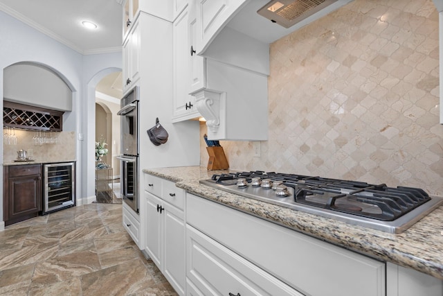 kitchen featuring beverage cooler, white cabinetry, appliances with stainless steel finishes, light stone countertops, and crown molding