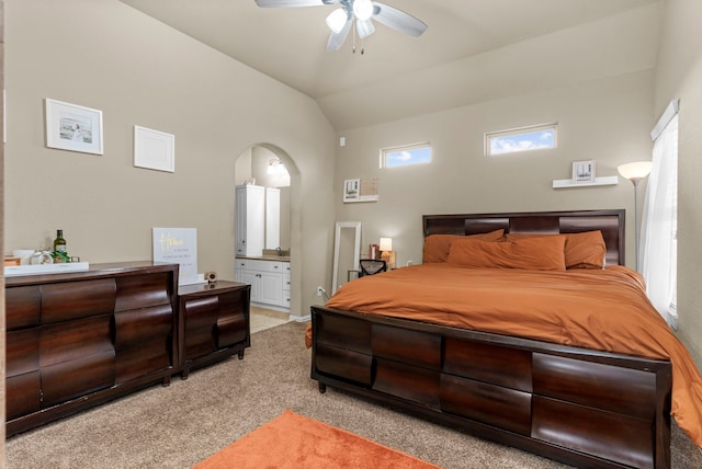 bedroom featuring ensuite bathroom, arched walkways, light colored carpet, a ceiling fan, and vaulted ceiling