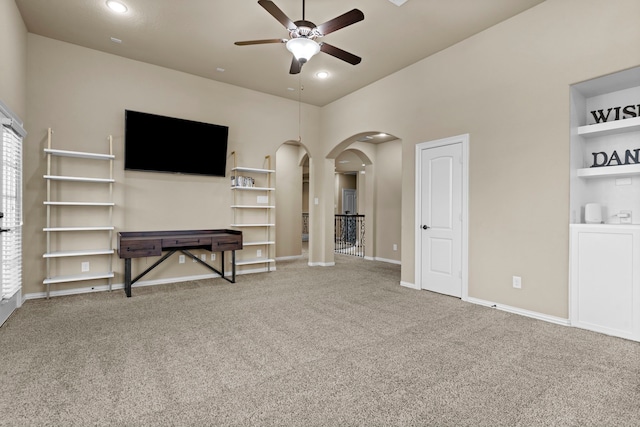 unfurnished living room with a ceiling fan, arched walkways, carpet flooring, and baseboards