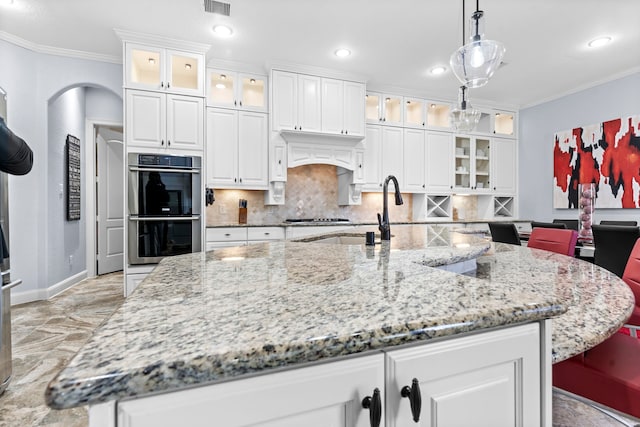 kitchen with hanging light fixtures, glass insert cabinets, double oven, white cabinets, and a sink