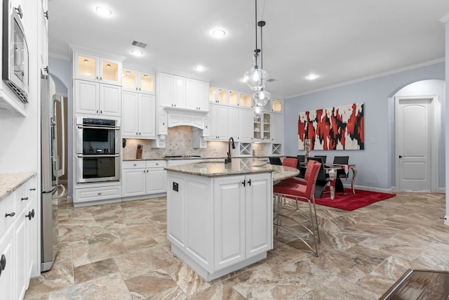 kitchen featuring arched walkways, white cabinets, appliances with stainless steel finishes, glass insert cabinets, and light stone counters