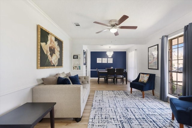 living area featuring light wood finished floors, baseboards, visible vents, crown molding, and ceiling fan with notable chandelier