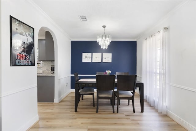 dining area with ornamental molding, light wood finished floors, visible vents, and a notable chandelier