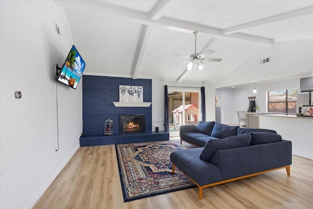 living room with vaulted ceiling with beams, wood finished floors, visible vents, a ceiling fan, and a brick fireplace