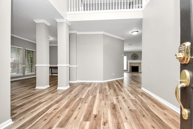 entryway featuring baseboards, wood finished floors, crown molding, ornate columns, and a fireplace