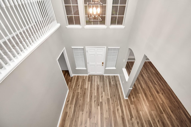 entryway with a notable chandelier, wood finished floors, a towering ceiling, baseboards, and stairs