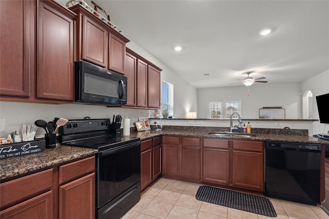 kitchen featuring light tile patterned floors, a sink, dark stone countertops, a peninsula, and black appliances