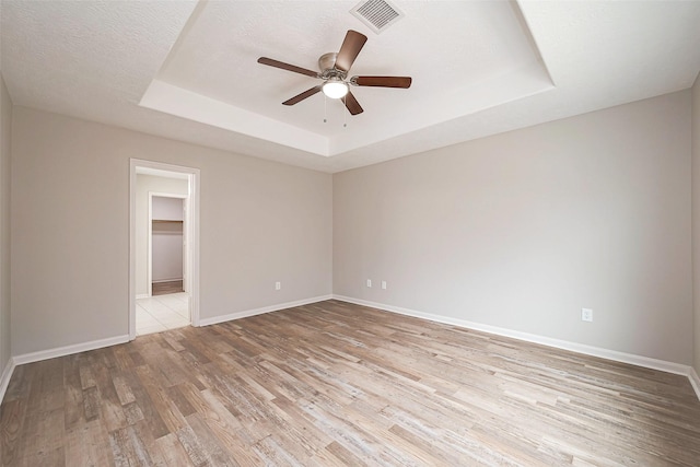 spare room with baseboards, visible vents, a raised ceiling, ceiling fan, and light wood-style floors