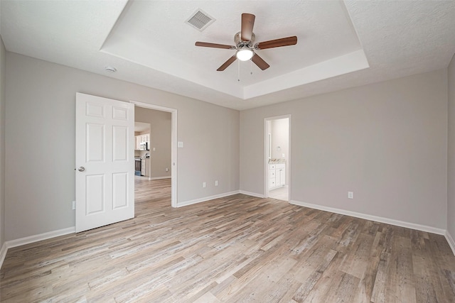 unfurnished room with light wood-type flooring, baseboards, visible vents, and a raised ceiling