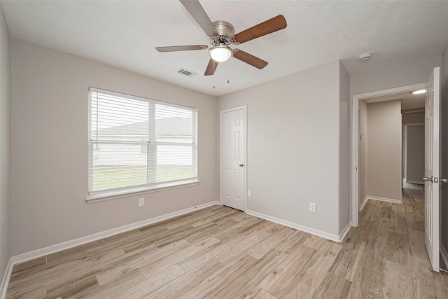 spare room featuring ceiling fan, a textured ceiling, visible vents, baseboards, and light wood-style floors