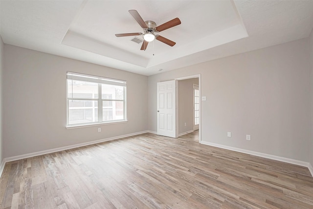 unfurnished bedroom featuring a tray ceiling, light wood-style flooring, and baseboards