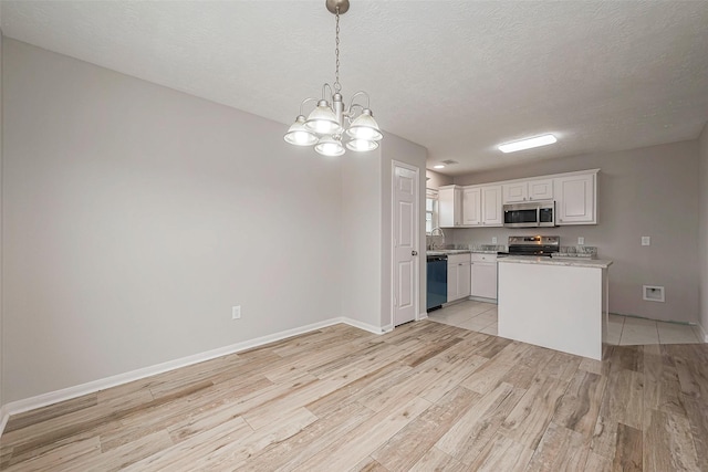 kitchen featuring light wood finished floors, stainless steel appliances, light countertops, white cabinets, and a textured ceiling