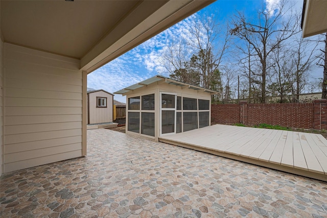 wooden deck featuring a patio area, an outdoor structure, fence, and a sunroom