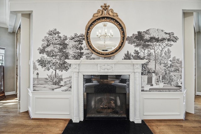 room details featuring wood finished floors, a decorative wall, a fireplace with flush hearth, and an inviting chandelier