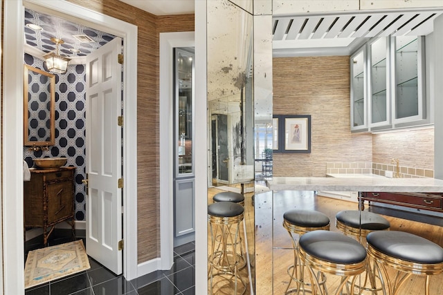 kitchen with wallpapered walls, dark tile patterned flooring, glass insert cabinets, an inviting chandelier, and light countertops