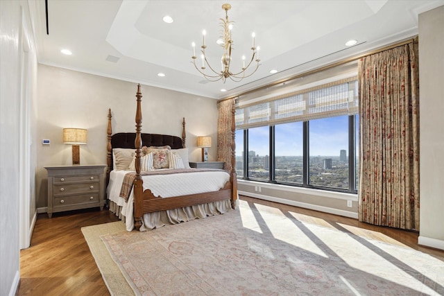 bedroom featuring baseboards, a view of city, light wood finished floors, a raised ceiling, and crown molding