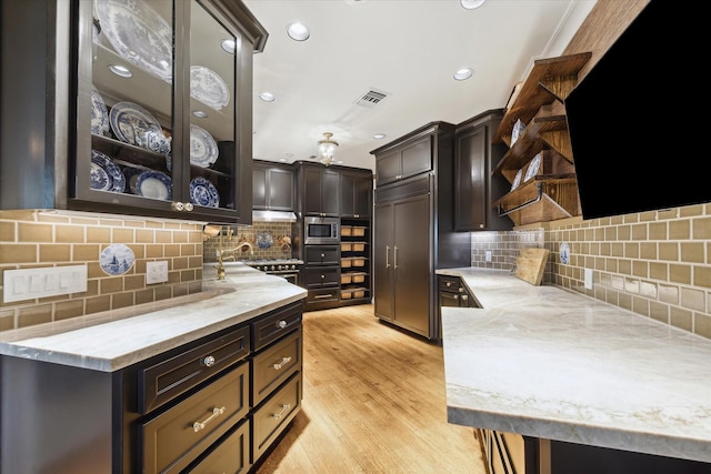 kitchen with glass insert cabinets, visible vents, dark brown cabinets, and built in appliances