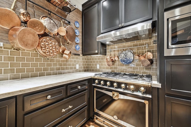 kitchen featuring light stone counters, dark brown cabinets, appliances with stainless steel finishes, ventilation hood, and backsplash