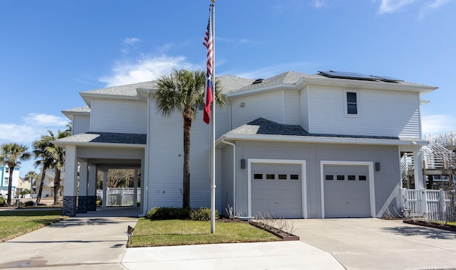 view of front of property with a shingled roof, roof mounted solar panels, fence, and concrete driveway