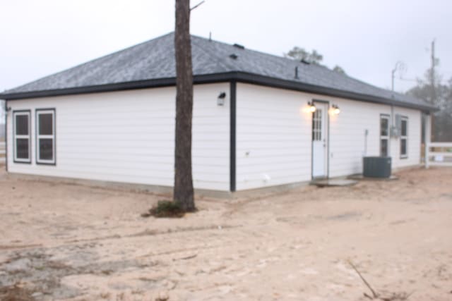 exterior space featuring a shingled roof, dirt driveway, and cooling unit