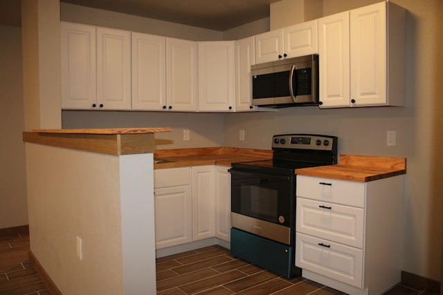 kitchen featuring wood finish floors, stainless steel microwave, electric range oven, white cabinetry, and butcher block countertops