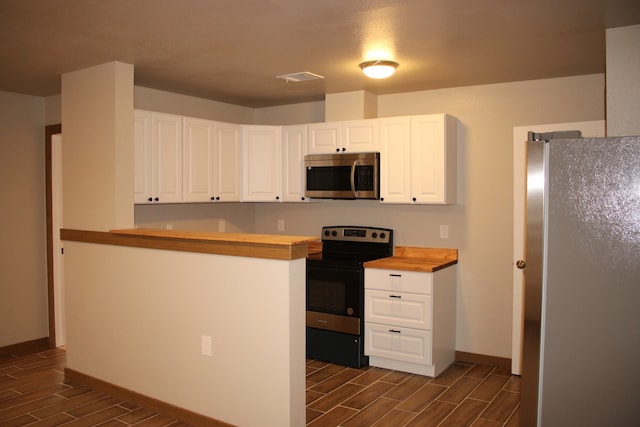 kitchen featuring appliances with stainless steel finishes, wood finish floors, butcher block counters, and white cabinets