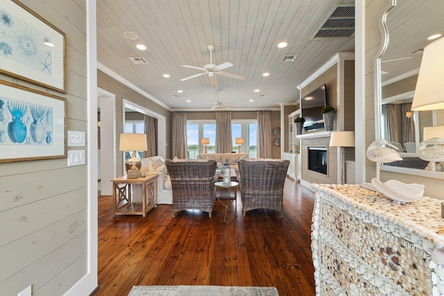 interior space featuring dark wood-style flooring, wood ceiling, visible vents, ornamental molding, and a glass covered fireplace