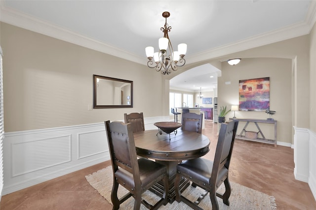 tiled dining space with ornamental molding, arched walkways, a wainscoted wall, and an inviting chandelier